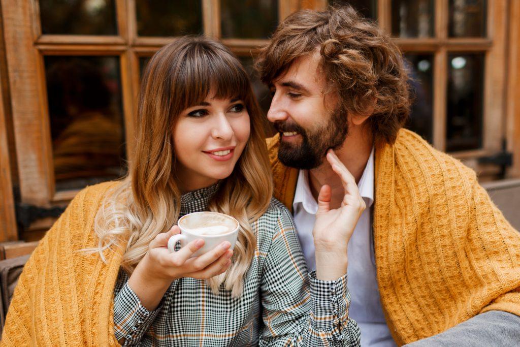 Close up cozy warm portrait of happy hugging couple in love. Handsome man and pretty woman having breakfast and drinking coffee on terrace.